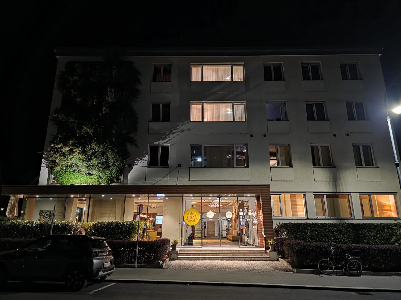 Beleuchteter Haupteingang des At the Park Hotels am Kaiser-Franz-Ring in Baden bei Nacht, mit dem gelben Hotellogo über der Glastür