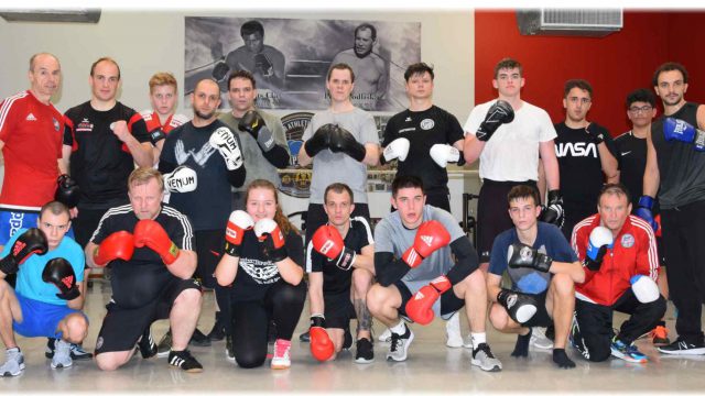 Trainingsgruppe des Badener AC Boxen mit Boxhandschuhen im Trainingsraum, im Hintergrund ein Plakat zu Ehren von Peter Podliska