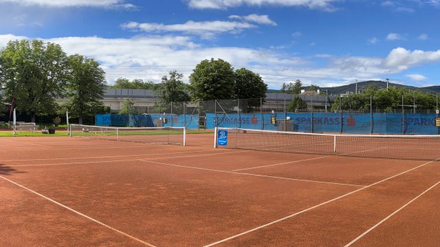 Sandplätze des Badener AC Tennis in der Dammgasse in Baden an einem sonnigen Tag, im Hintergrund Bäume und Hügel