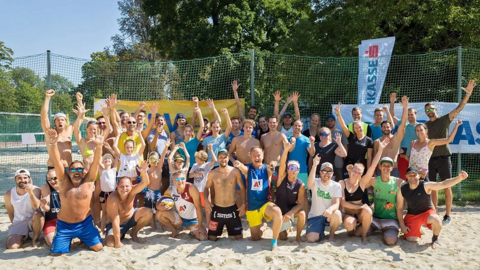 Gruppenfoto des 1. Badener Beachvolleyball Vereins: rund 50 Spielerinnen und Spieler jubeln auf dem Sand eines Courts im Strandbad Baden