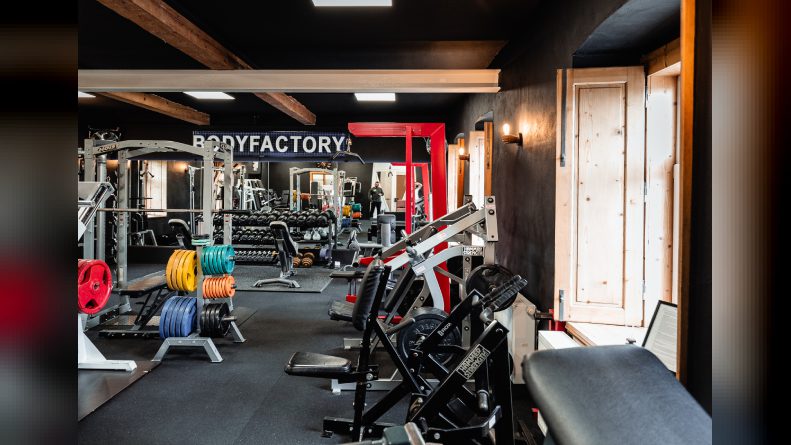 Trainingsraum der BodyFactory in Tribuswinkel mit Plate-Load-Maschinen, bunten Hantelscheiben, Racks und Holzbalkendecke