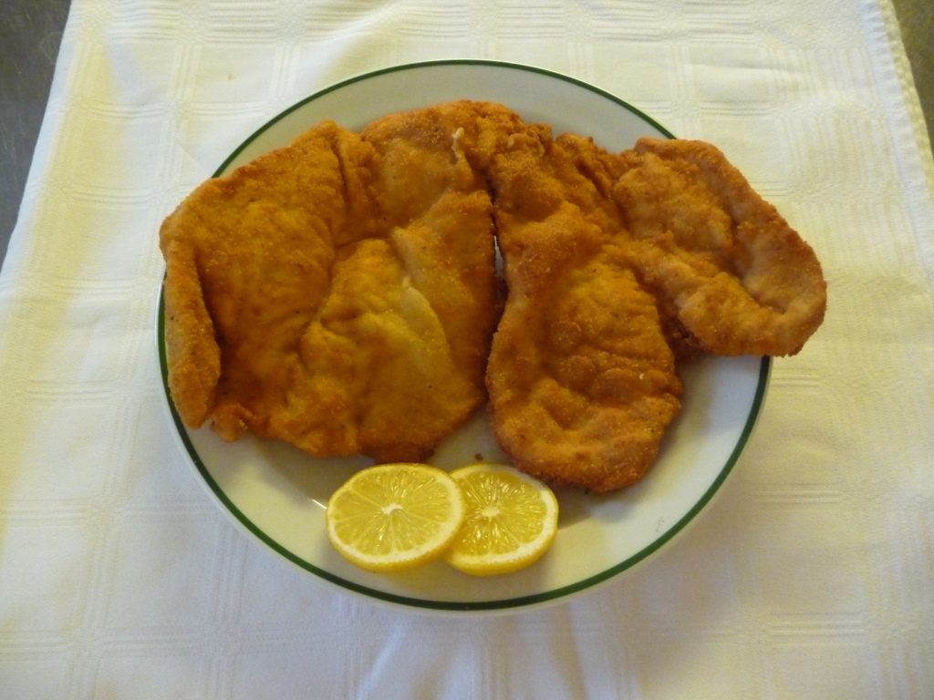 Zwei gebackene Hühnerfilets mit Zitronenscheiben auf einem weißen Teller mit grünem Rand