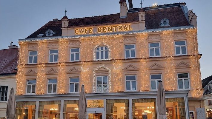 Das Café Central am Hauptplatz in Baden in der Abenddämmerung: zweistöckige Fassade mit goldenem Schriftzug und Lichterketten über der Front