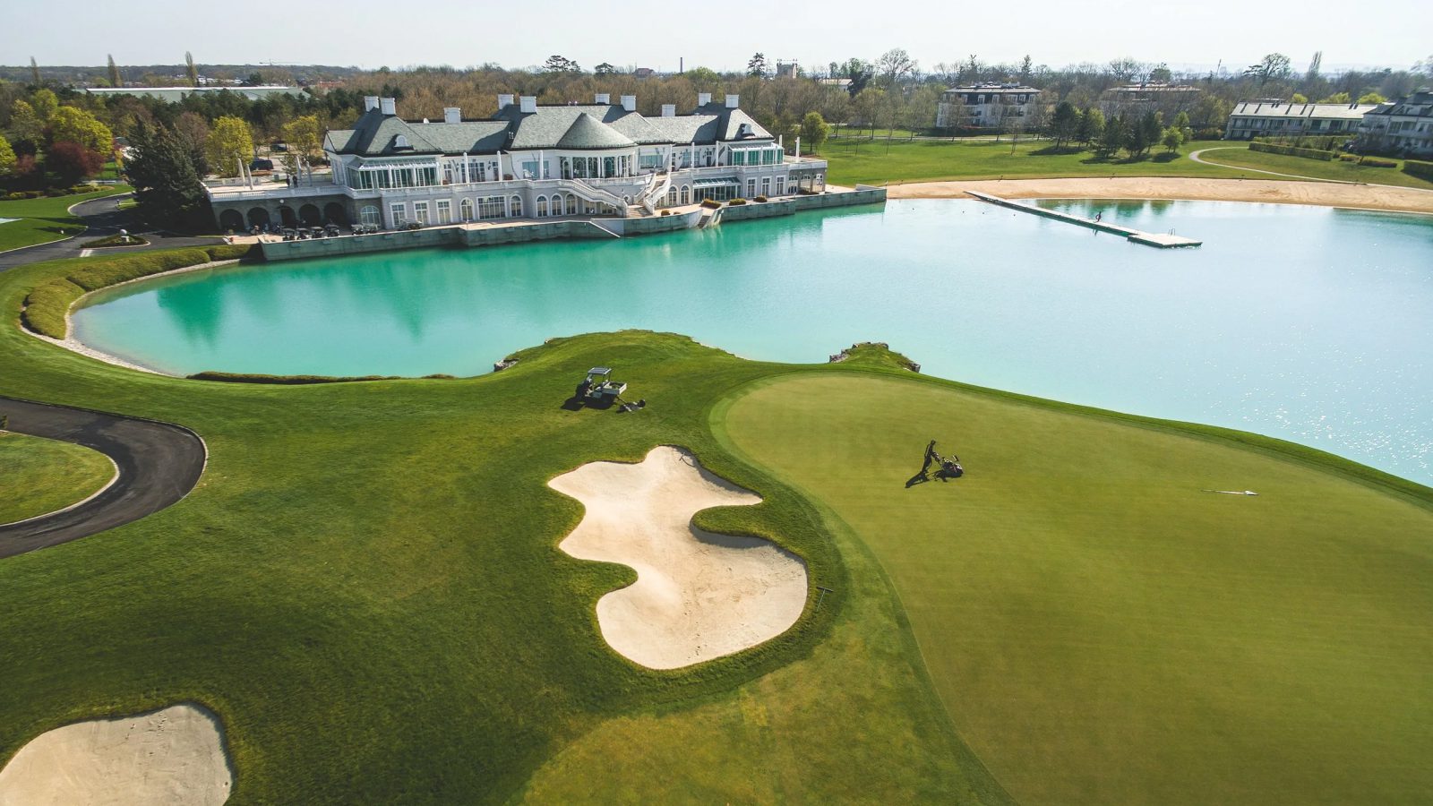 Golfplatz FONTANA in Oberwaltersdorf von oben: Grün mit Sandbunkern, türkiser Badesee mit Steg und das weiße Clubhaus