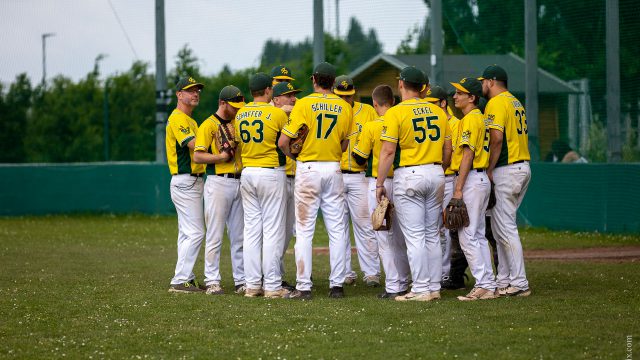 Spieler der Grasshoppers Traiskirchen in gelben Trikots und weißen Hosen stehen auf dem Spielfeld zur Besprechung zusammen