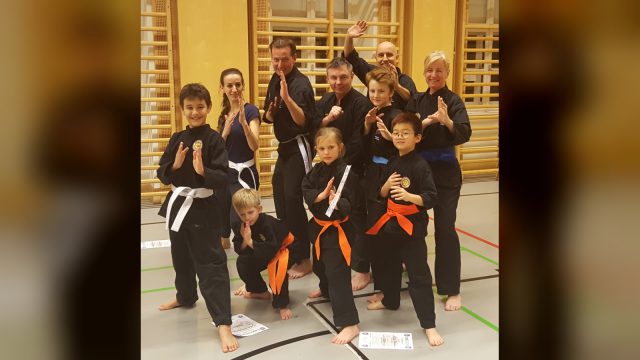 Silat-Gruppe der JOANDO Kampfsportschule nach der Gürtelprüfung: Kinder und Erwachsene in schwarzen Anzügen posieren im Turnsaal