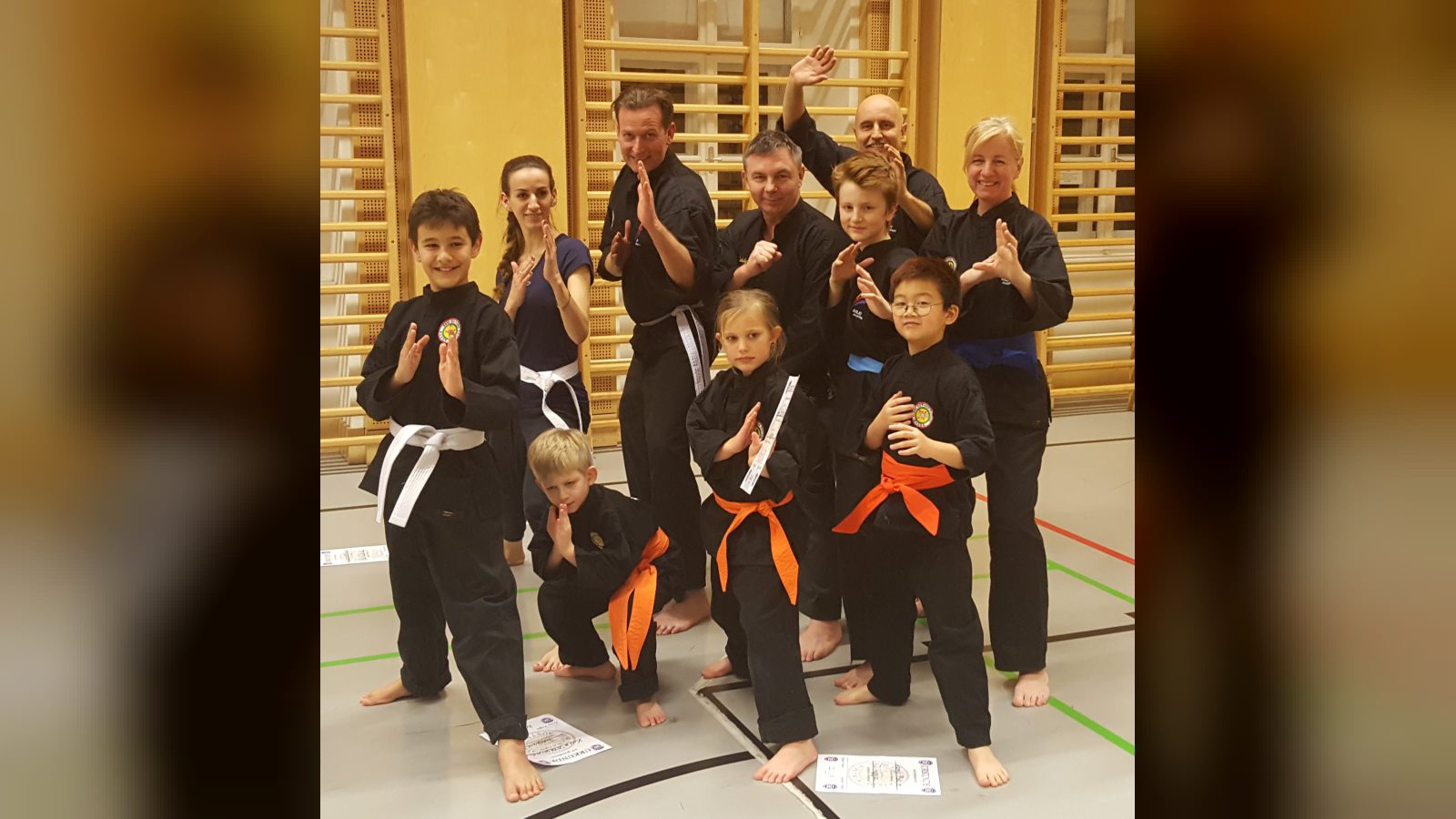 Silat-Gruppe der JOANDO Kampfsportschule nach der Gürtelprüfung: Kinder und Erwachsene in schwarzen Anzügen posieren im Turnsaal