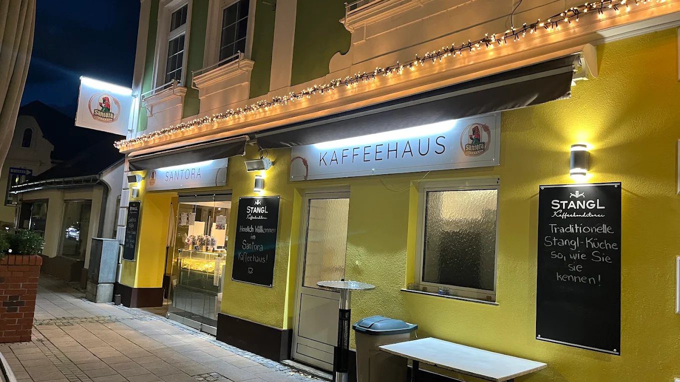 Gelbe Hausfassade in der Berndorfer Fußgängerzone am Abend, mit Lichterkette, beleuchtetem Kaffeehaus-Schild und zwei Kreidetafeln vor dem Eingang