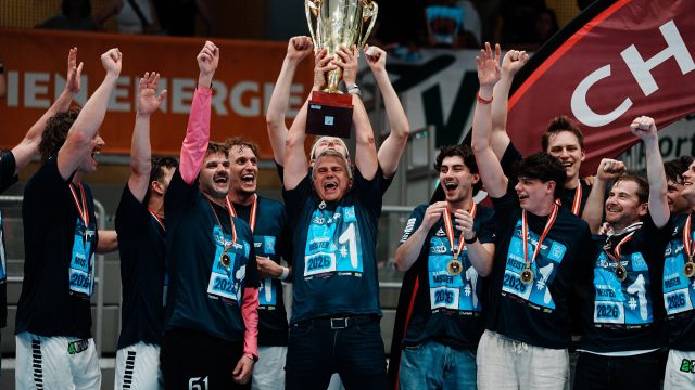 Spieler von roomz JAGS Vöslau feiern mit Medaillen und Meister-Shirts den HLA-Meistertitel 2026, in der Mitte wird der Pokal hochgehalten