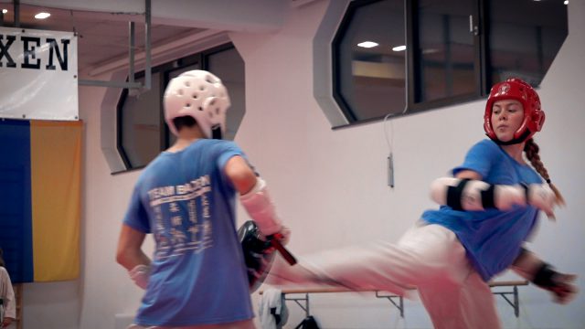 Taekwondo-Training beim TEAM BADEN: Sportlerin mit rotem Kopfschutz tritt gegen eine Pratze, die ihr Trainingspartner mit weißem Helm hält