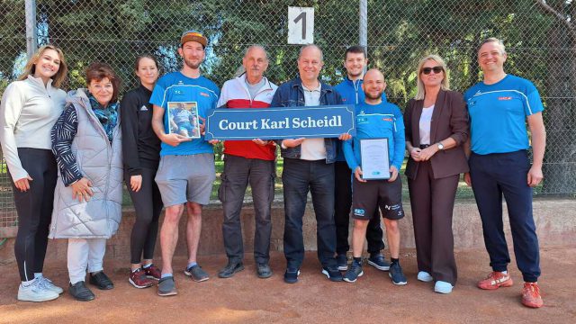 Vereinsmitglieder des TC Oberwaltersdorf stehen auf dem Sandplatz 1 und halten die neue Tafel „Court Karl Scheidl“ und ein gerahmtes Foto des Gründers