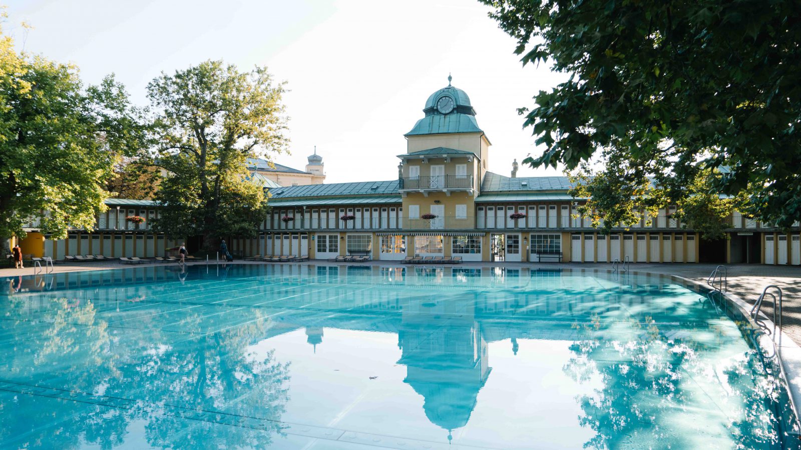 Becken im Thermalbad Vöslau, in dem sich das historische gelbe Badgebäude mit Uhrturm und den Kabanenreihen spiegelt