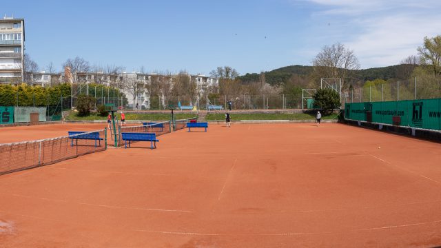 Tennisanlage des UNION LTC Berndorf: rote Sandplätze mit Netzen und blauen Bänken, dahinter Wohnhäuser und bewaldete Hügel