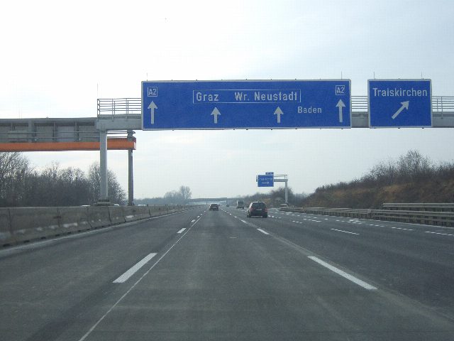 Autobahn mit blauen Wegweisern auf einer Schilderbrücke: geradeaus Graz, Wiener Neustadt und Baden, rechts die Ausfahrt Traiskirchen