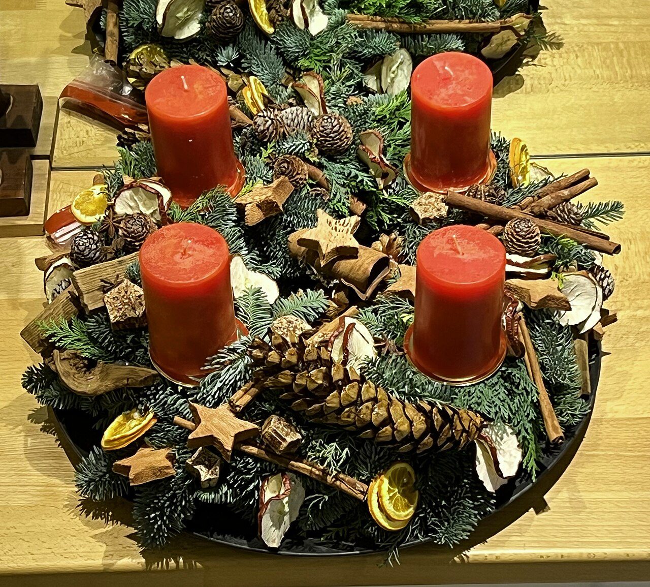 Ein Adventkranz aus Tannenzweigen mit vier roten Kerzen, geschmückt mit Zapfen, Zimtstangen, getrockneten Orangen- und Apfelscheiben
