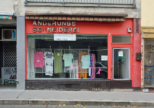 Rote Ladenfront einer Änderungsschneiderei in Wien-Rudolfsheim mit Blusen und Kleidern auf Bügeln im Schaufenster