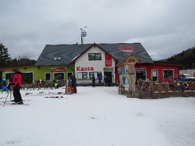 Kassa und Skiverleih der Annaberger Lifte im Schnee, davor Skifahrer und abgestellte Ski