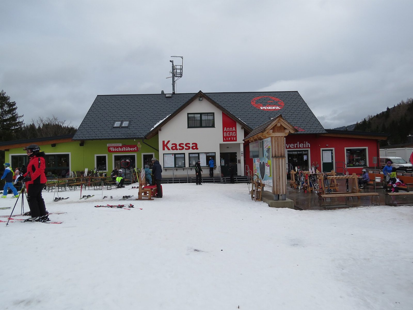 Kassa und Skiverleih der Annaberger Lifte im Schnee, davor Skifahrer und abgestellte Ski