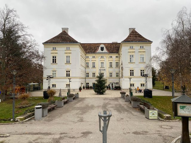 Rathaus Bad Vöslau, ein weißes Schloss mit zwei Ecktürmen im Schlosspark, davor ein Christbaum und ein Weg mit Bänken