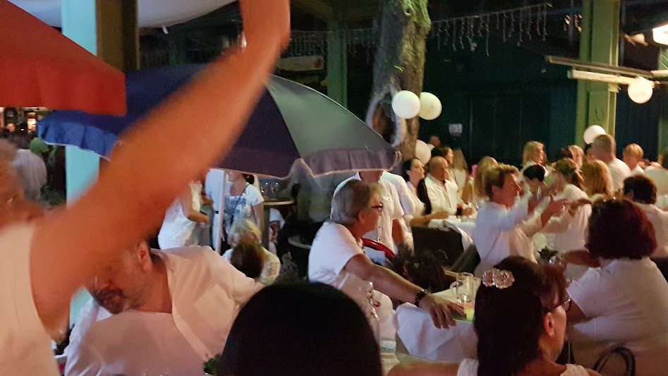 Gäste in weißer Kleidung feiern am Abend an gedeckten Tischen unter Schirmen und weißen Lampions