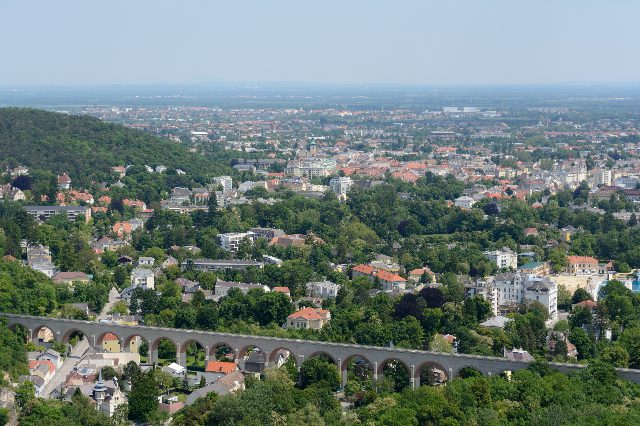 Blick über Baden bis ins Wiener Becken: Villen im Grünen, die Häuser der Innenstadt und vorne die Bögen des Aquädukts der Wiener Hochquellenwasserleitung