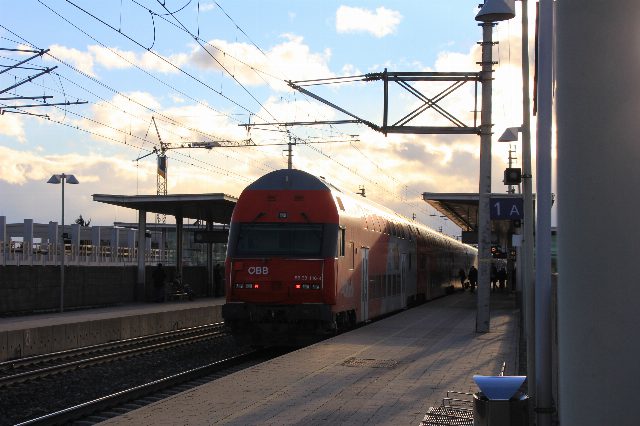 Roter Doppelstock-Wendezug der ÖBB am Bahnsteig des Bahnhofs Baden im Abendlicht, darüber Oberleitungen
