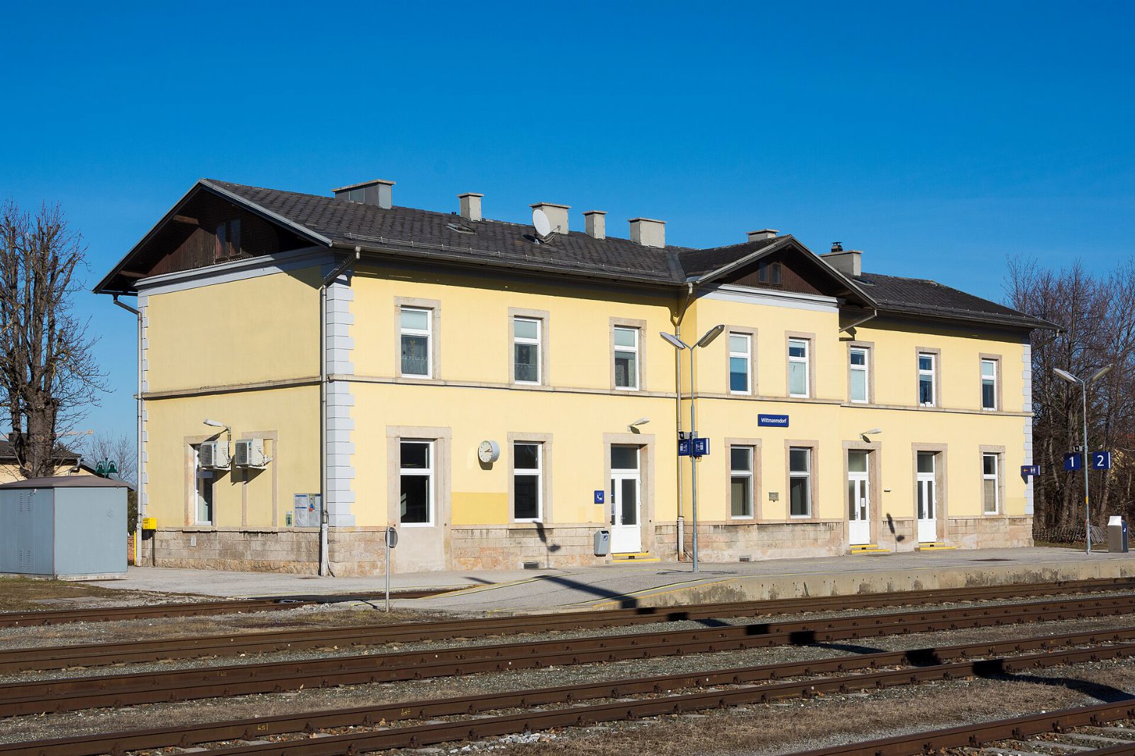 Gelbes Bahnhofsgebäude Wittmannsdorf mit Bahnsteig und Gleisen vor blauem Himmel