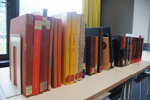 Symbolbild: eine Reihe Bücher mit roten, gelben und schwarzen Einbänden auf einem Tisch