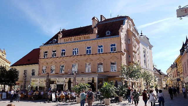 Das Café Central am Hauptplatz in Baden an einem sonnigen Tag: Fassade mit goldenem Schriftzug „CAFE CENTRAL“ unter dem Dach, davor ein voller Schanigarten und Passanten