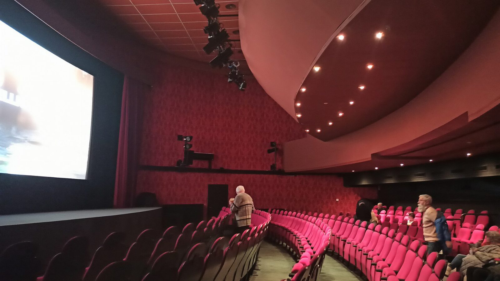 Kinosaal des Cinema Paradiso Baden mit roten Sitzreihen in einem Bogen, links die beleuchtete Leinwand