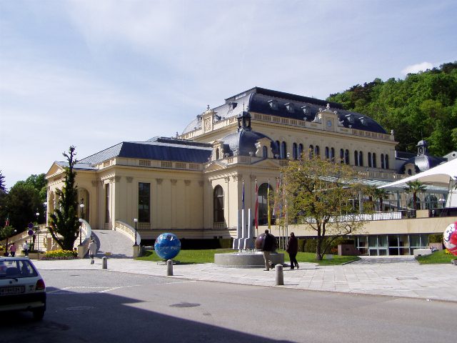 Congress Casino Baden von außen, heller Prachtbau mit dunklem Mansarddach, davor ein Brunnen und Passanten