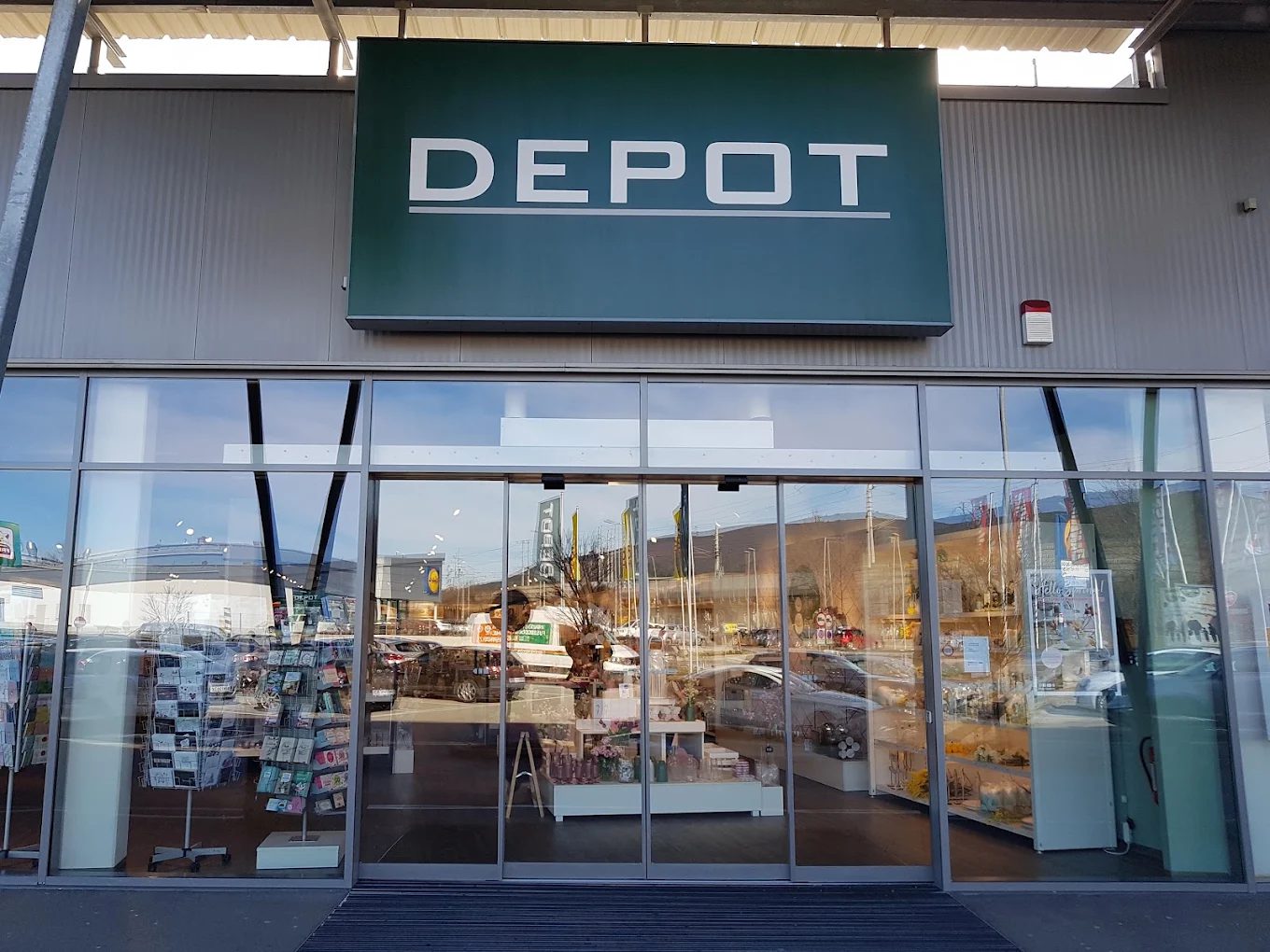 Eingang der früheren DEPOT-Filiale in Baden mit grünem DEPOT-Schild über einer Glasfront, dahinter Regale mit Deko und Grußkarten