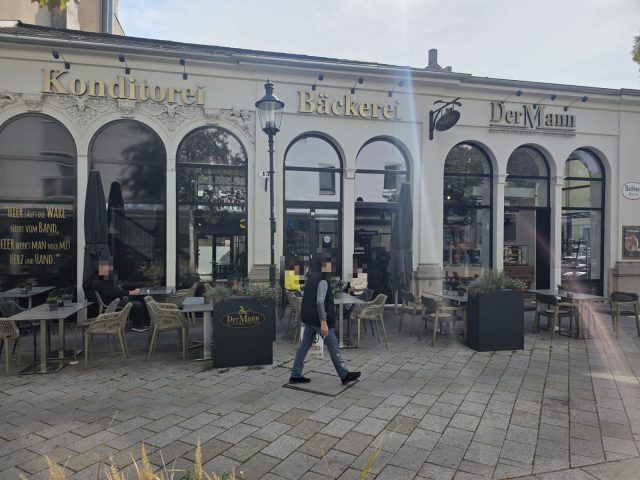Fassade der Filiale in der Rathausgasse 13 in Baden mit Rundbogenfenstern, den goldenen Schriftzügen Konditorei, Bäckerei und DerMann und dem Schanigarten davor