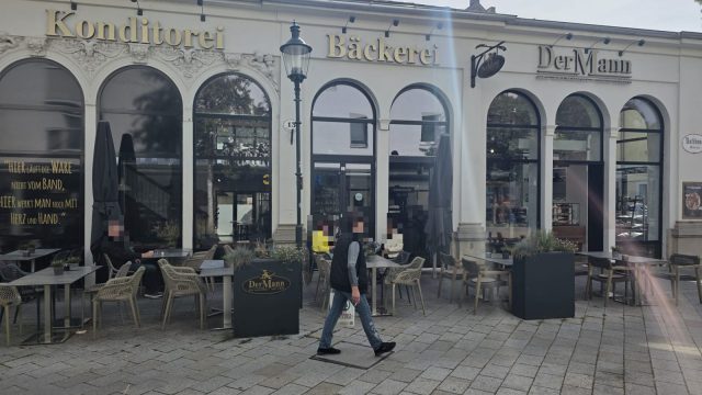 Die Filiale von Der Mann in der Rathausgasse 13 in Baden: helles Haus mit Rundbogenfenstern, darüber die goldenen Schriftzüge Konditorei, Bäckerei und DerMann, davor der Schanigarten