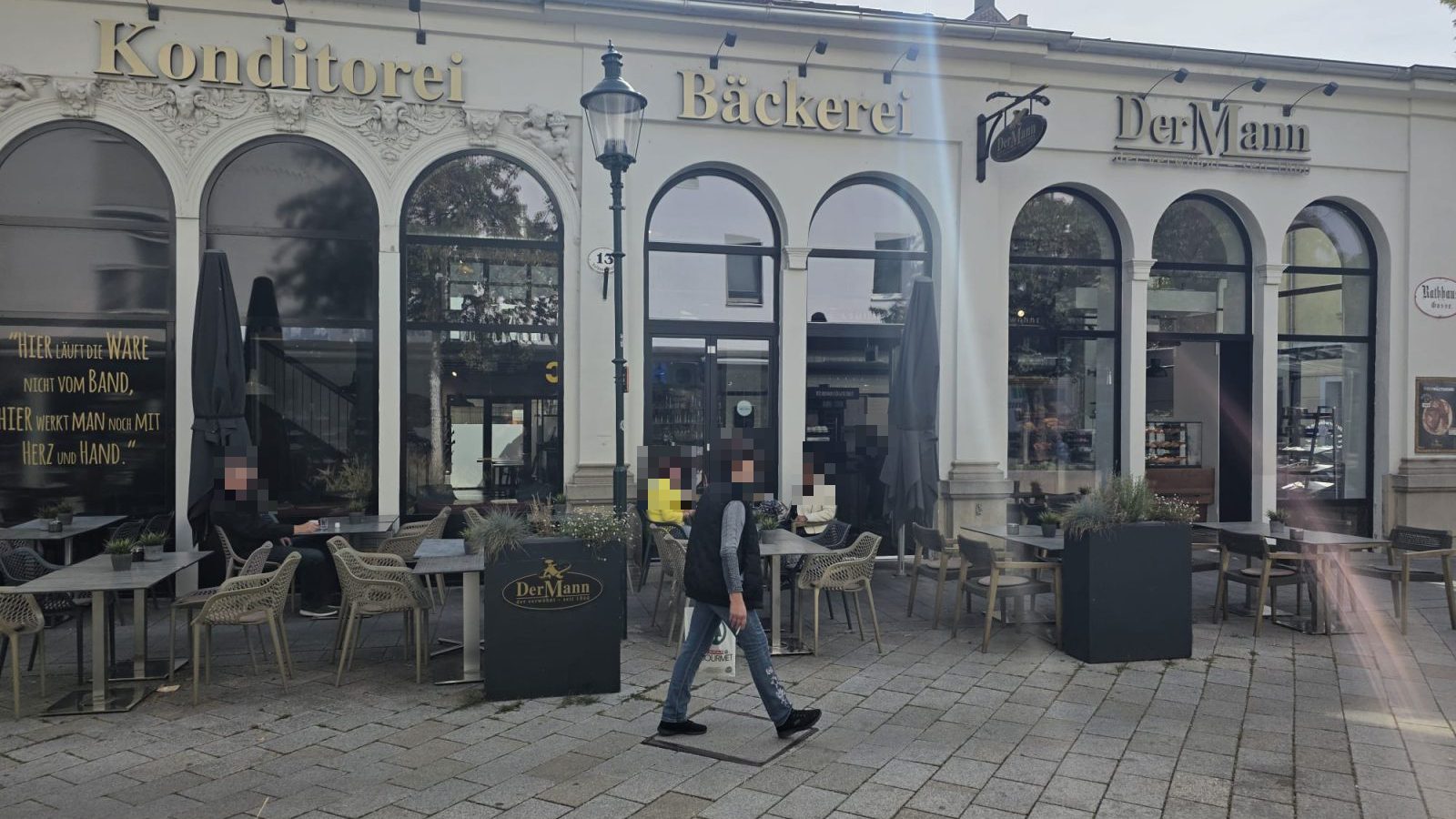 Die Filiale von Der Mann in der Rathausgasse 13 in Baden: helles Haus mit Rundbogenfenstern, darüber die goldenen Schriftzüge Konditorei, Bäckerei und DerMann, davor der Schanigarten