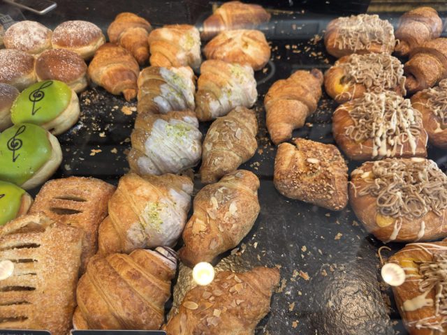 Blick in die Vitrine: Croissants mit Mandelblättchen, gefüllte Plunderstücke, Krapfen mit Staubzucker und grün glasierte Krapfen mit Notenschlüssel
