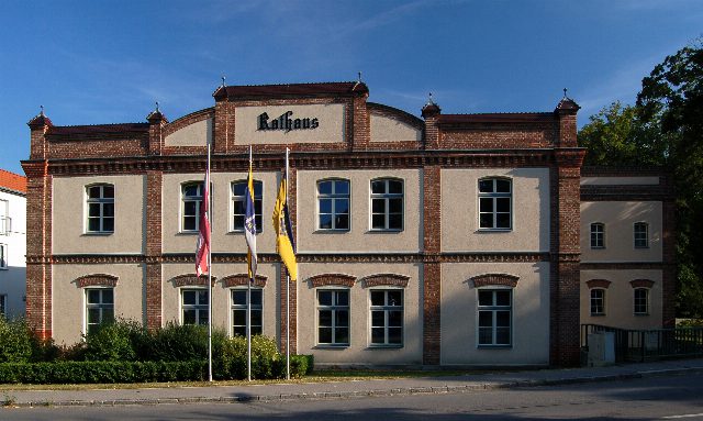 Rathaus Ebreichsdorf, zweistöckiger Bau mit Ziegelgliederung und Schriftzug Rathaus, davor drei Fahnen