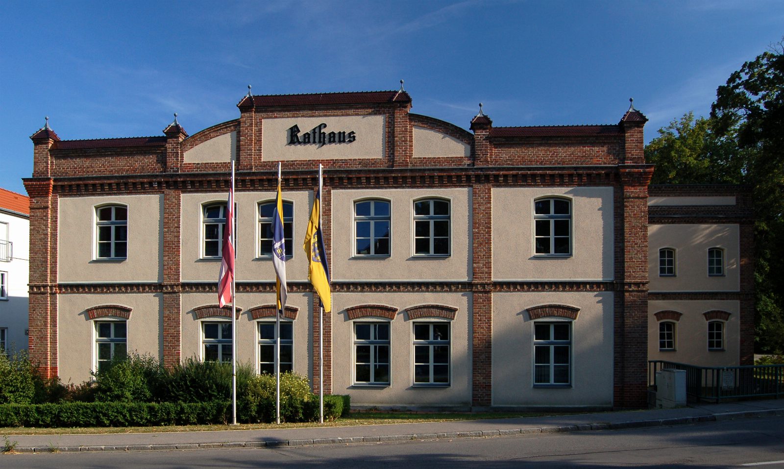 Rathaus Ebreichsdorf, zweistöckiger Bau mit Ziegelgliederung und Schriftzug Rathaus, davor drei Fahnen
