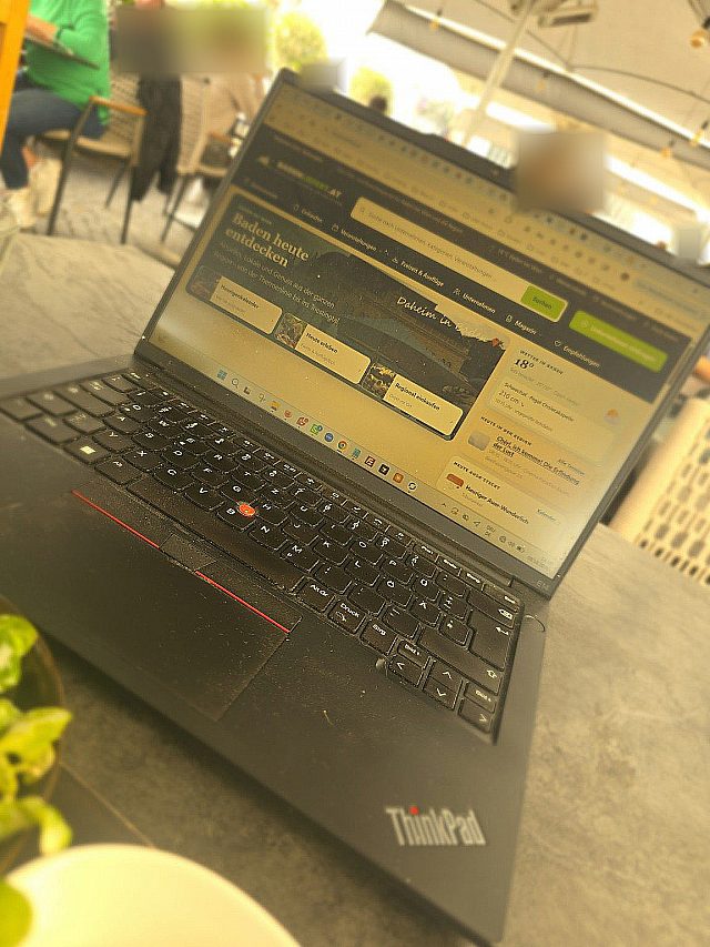 Aufgeklappter Laptop auf einem Tisch im Schanigarten, am Bildschirm die Startseite von badenliefert.at mit „Baden heute entdecken“