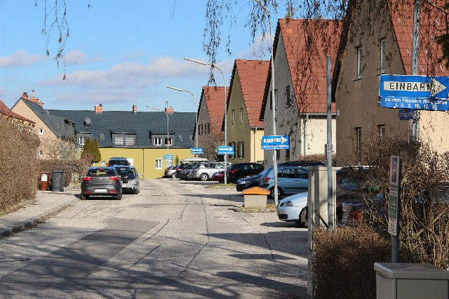 Wohnstraße in Enzesfeld mit Häusern mit roten Satteldächern, parkenden Autos und blauen Einbahnschildern