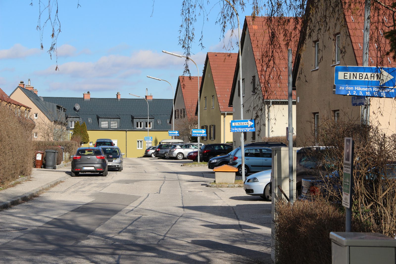 Wohnstraße in Enzesfeld mit Häusern mit roten Satteldächern, parkenden Autos und blauen Einbahnschildern