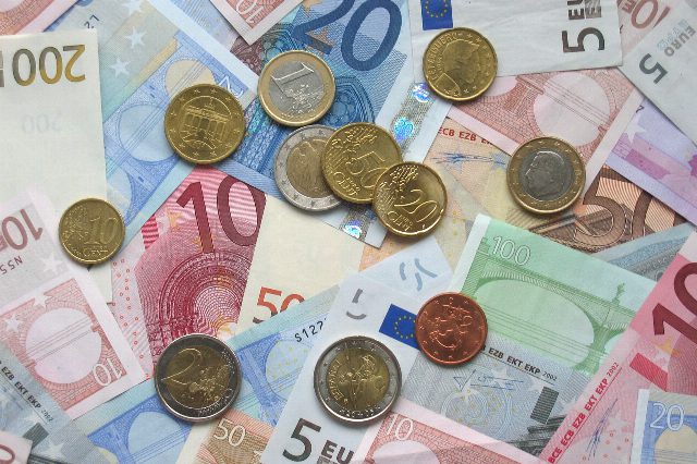 Durcheinanderliegende Euroscheine von 5 bis 200 Euro, darauf verstreut Euromünzen verschiedener Länder