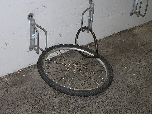 Ein einzelnes Vorderrad hängt mit einem Bügelschloss an einem Fahrradständer an der Wand, der Rest des Rads ist weg