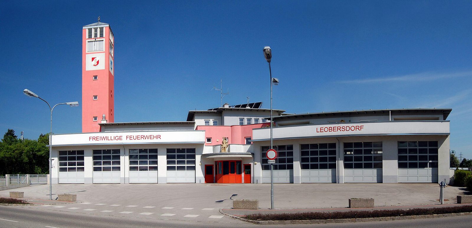 Feuerwehrhaus der Freiwilligen Feuerwehr Leobersdorf mit Fahrzeughallen und dem rosa Feuerwehrturm links, davor der leere Vorplatz