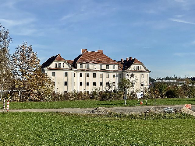 Gebäude des Finanzamts Österreich, Dienststelle Waldviertel, in Gmünd: dreistöckiger heller Bau mit rotem Walmdach hinter herbstlichen Bäumen und einer Wiese