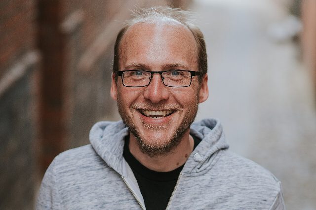 Florian Freistetter mit Brille und grauer Kapuzenjacke lacht in die Kamera