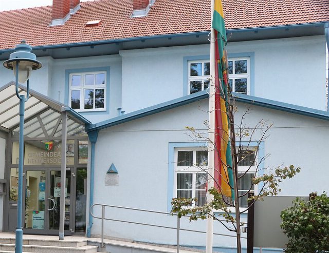 Gemeindeamt Hennersdorf: hellblaues Haus mit Glasvordach über dem Eingang, Schriftzug „Gemeindeamt Hennersdorf“ und Fahnenmast davor