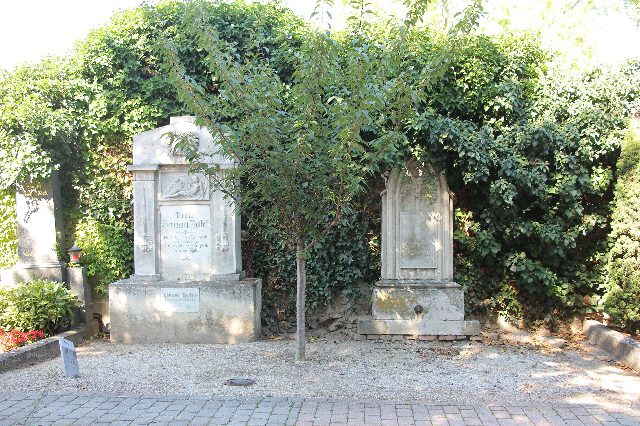 Steinernes Grabmal der Familie Hermann Rollett vor einer efeubewachsenen Mauer, daneben ein zweiter alter Grabstein