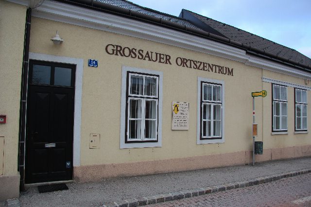 Gelbes ebenerdiges Haus mit dem Schriftzug Grossauer Ortszentrum, daneben eine Bushaltestelle