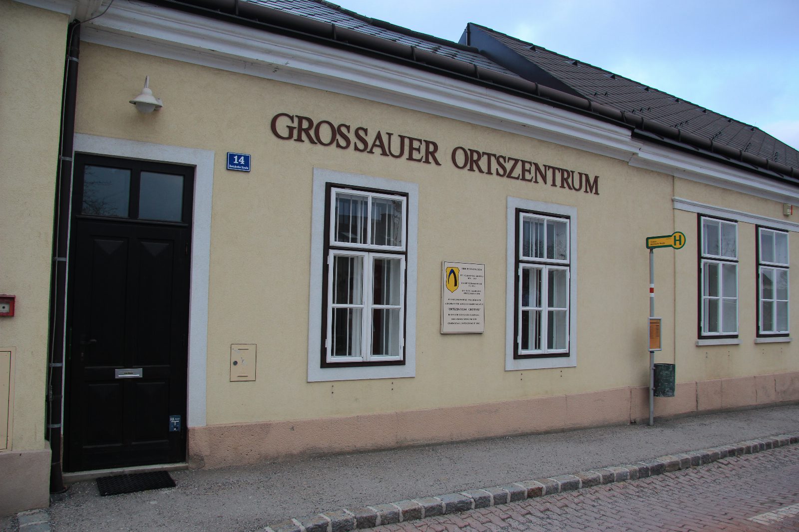 Gelbes ebenerdiges Haus mit dem Schriftzug Grossauer Ortszentrum, daneben eine Bushaltestelle